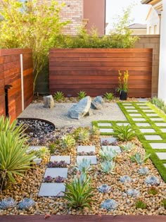 a small garden with rocks, grass and plants in the middle of it is next to a wooden fence