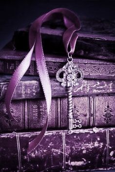 an old book with a key on it and a purple ribbon hanging from the front