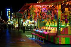 an amusement park at night with lights and decorations on the stalls, including teddy bears