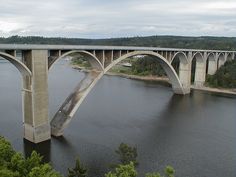 a large bridge spanning over a river next to a forest