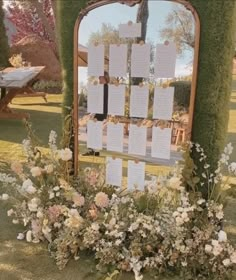 a mirror sitting on top of a lush green field next to flowers and plants in front of it