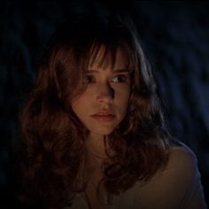 a woman with long brown hair and blue eyes stares into the distance in a dark room