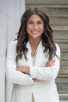 a woman with her arms crossed standing next to a white wall wearing a white blazer