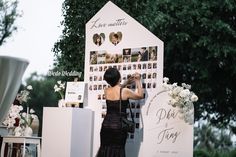 a woman standing in front of a sign with pictures on it and flowers hanging from the wall