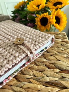 a crocheted notebook sitting on top of a wicker basket next to sunflowers