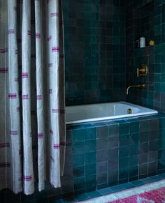 a bath tub sitting under a window next to a shower curtain with pink and blue stripes on it