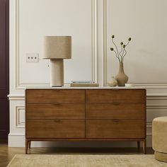 a wooden dresser sitting next to a lamp on top of a table in a room