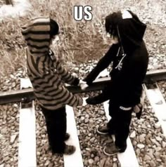 two young boys are standing on railroad tracks and one is holding the hand of another boy