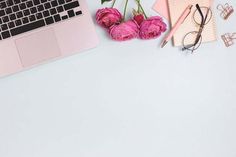 an open laptop computer sitting on top of a desk next to pink flowers and eyeglasses