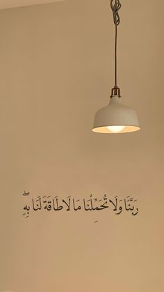 a lamp hanging from the ceiling above a bed in a room with arabic writing on the wall