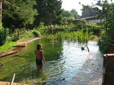 a woman standing in the middle of a pool surrounded by lush green plants and trees