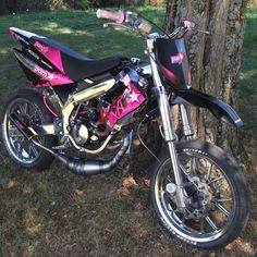 a pink and black motorcycle parked next to a tree