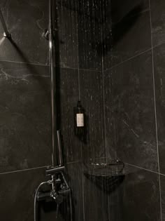 a shower head with rain coming from it in a black tiled bathroom wall and floor