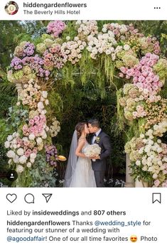 the bride and groom are kissing under a floral arch