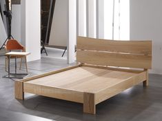 a wooden bed frame sitting on top of a hard wood floor next to a chair