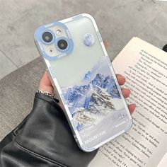 a person holding a book with a phone case on their hand and an open book in front of them