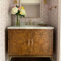 a bathroom vanity with marble counter top and wooden cabinet, flowers in vase on the sink