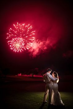 a bride and groom kissing in front of fireworks at their wedding reception on the lawn