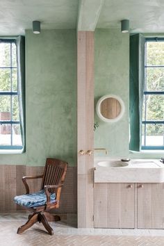 a chair sitting next to a sink in a room with green walls and two windows