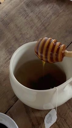 a cup of tea with a wooden spoon full of honey on the table next to it