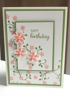 a birthday card with pink flowers and green trimmings on the front, sitting on a table