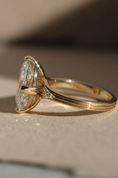 a yellow gold ring with a diamond on the top and side, sitting on a beige surface