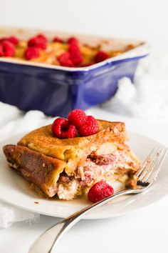 a white plate topped with french toast and raspberries next to a blue casserole dish