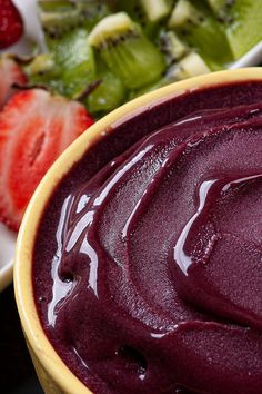 a close up of a bowl of food with fruit on the side and salad in the background