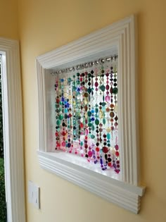 a white frame hanging on the side of a wall filled with colorful beads and chains