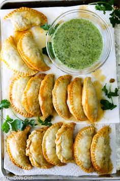 several pastries and a bowl of green sauce on a tray