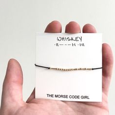 the morse code girl bracelet is in someone's hand and it says whiskey on it