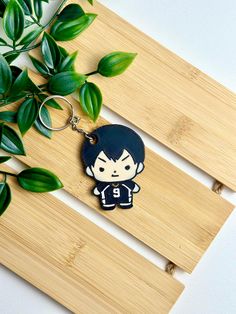 a keychain with a cartoon character on it sitting next to some plants and wood planks