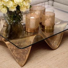 a glass table topped with candles and vase filled with white flowers next to a couch