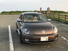 a brown car parked in a parking lot next to a wooden fence and grassy area