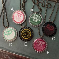 six bottle caps with names on them are hanging from a metal chain that is attached to a wall