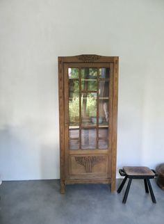 a wooden cabinet sitting in the corner of a room next to a stool and table