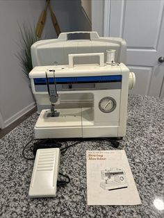 a white sewing machine sitting on top of a counter next to a manual for it