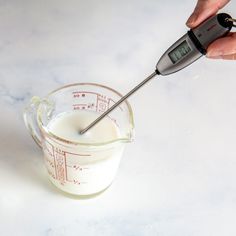 a hand holding a measuring cup filled with milk