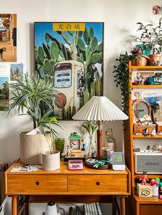 a wooden desk topped with a lamp next to a shelf filled with books and plants