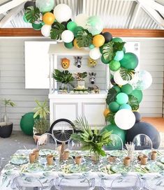 a table topped with lots of balloons and greenery next to a white cabinet filled with potted plants