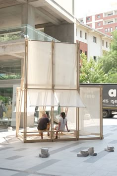 two people are sitting on a bench in front of a building with glass walls and windows