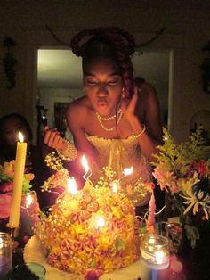 a woman blowing out candles on a birthday cake with flowers in front of her and other people around the table