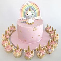 a pink cake with unicorns and cupcakes around it