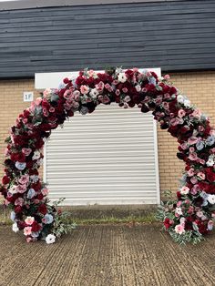 an arch made out of flowers and greenery in front of a brick building with a white garage door behind it