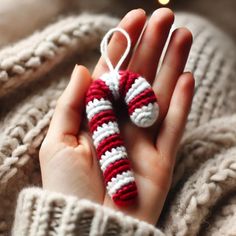 a hand holding a knitted christmas ornament in the shape of a candy cane