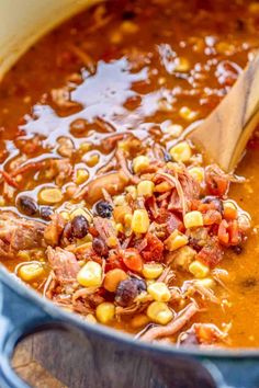 a pot filled with beans, corn and meat in a tomato broth sauce next to a wooden spoon