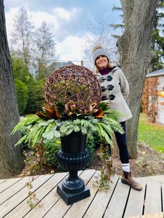 a woman standing on a wooden deck next to a planter with a ball in it