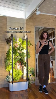 a woman standing in front of a vertical planter with plants growing on the wall