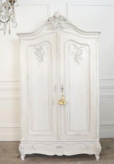 an antique white armoire with chandelier hanging from it's side, in front of a wall