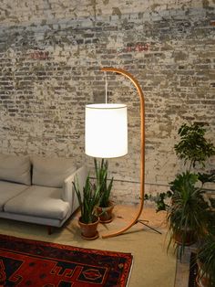 a living room with a couch, lamp and potted plants on the floor in front of a brick wall